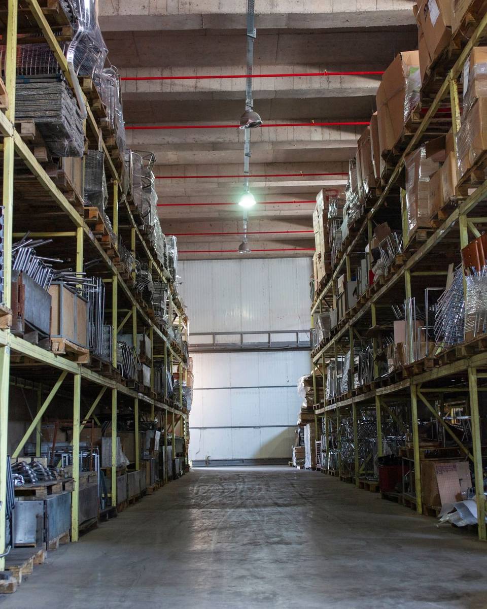 ممر مستودع مرتب بين رفوف معدنية عالية مليئة بالبضائع